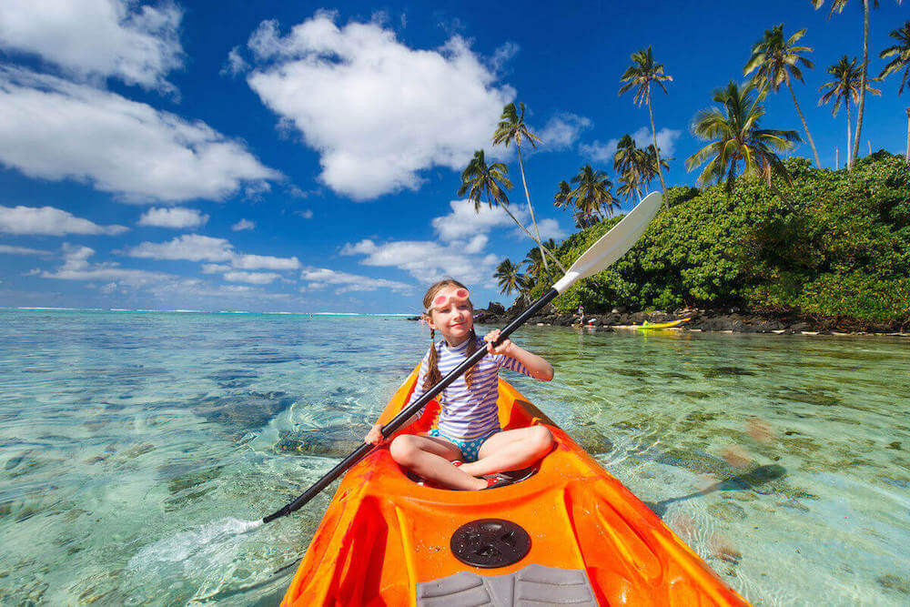 Find out the top tips for kayaking with kids in Hawaii by top Hawaii blog Hawaii Travel with Kids. Image of a girl with braided pigtails in an orange kayak in Hawaii.