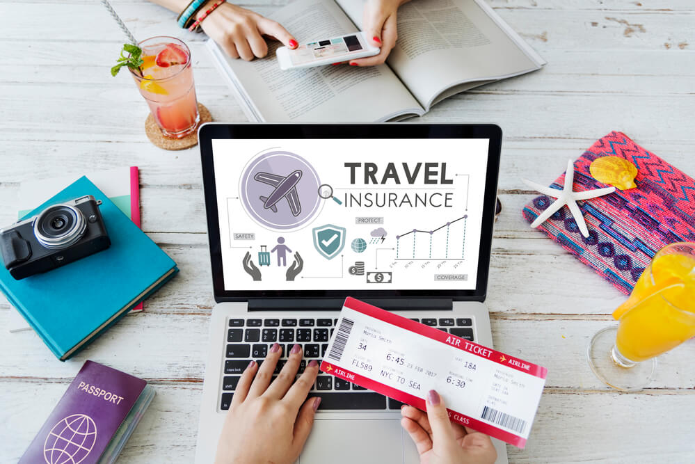 Find the right Hawaii travel insurance plan for your family. Image of a woman holding an airplane ticket in front of a laptop that says travel insurance on the screen.