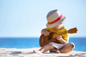 Find out where to find vacation babysitters in Hawaii recommended by top Hawaii blog Hawaii Travel with Kids. Imag eof a boy playing an ukulele on the beach.