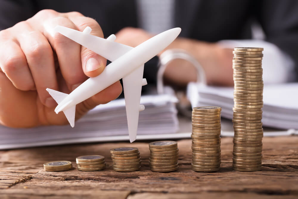 Find the right Hawaii travel insurance plan that fits your Hawaii budget. Image of someone holding a toy airplane next to stacks of coins.