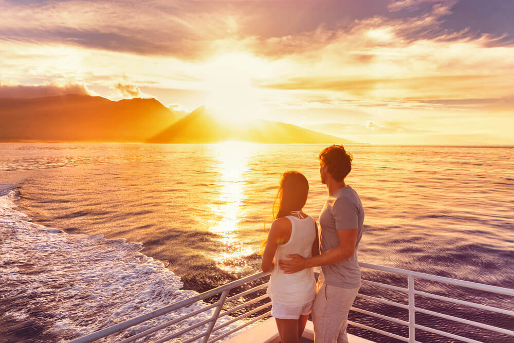 One of the coolest things to do on Maui at night is a sunset cruise. Image of a couple watching the Maui sunset from a boat.