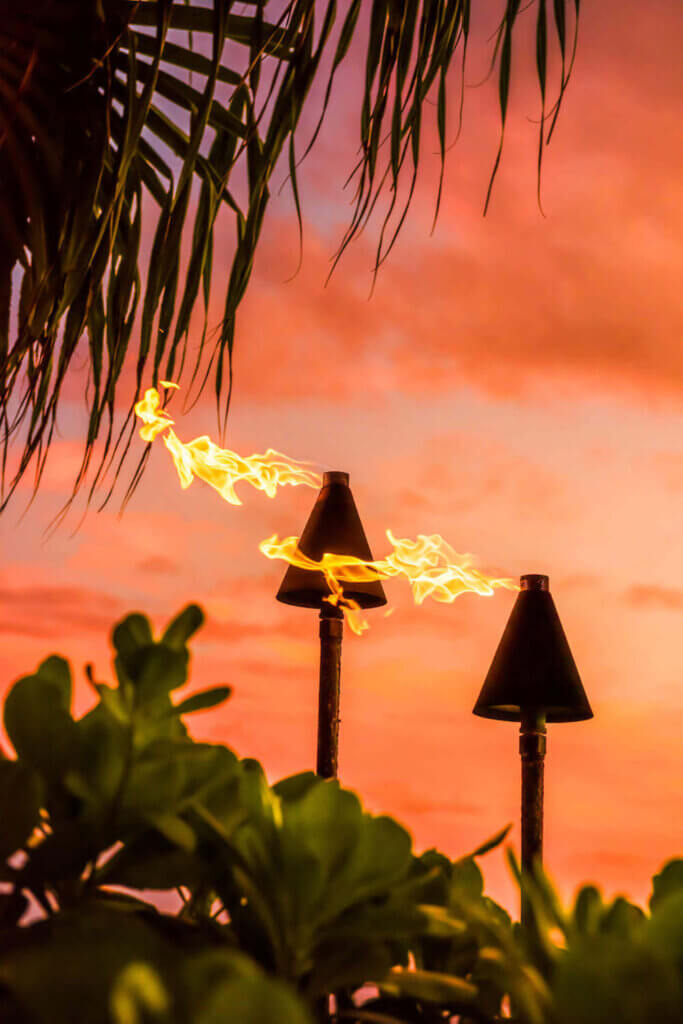 Watch the sunset on Maui while seeing a hula show. Image of tiki torches at sunset.