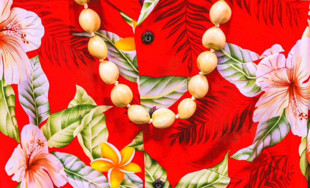 Find out the best Hawaii souvenirs worth buying according to top Hawaii blog Hawaii Travel with Kids. Image of a red Aloha shirt with a white kukui nut lei.