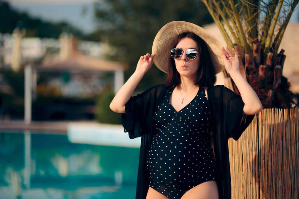 Find out what to wear in Hawaii while pregnant by top Hawaii blog Hawaii Travel with Kids. Image of a pregnant woman wearing sunglasses, a sun hat, maternity swimsuit, and coverup