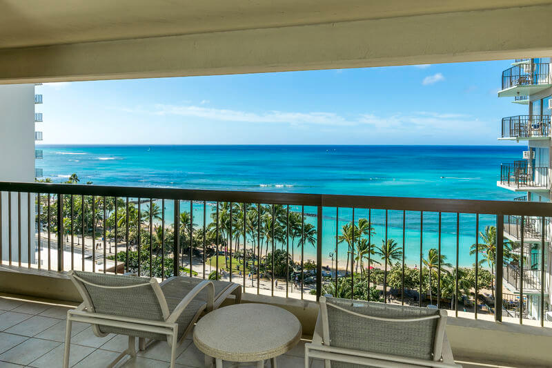 One of the best places to stay in Waikiki is the Aston Waikiki Beach Tower. Image of a lanai with a sweeping view of Waikiki beach and the Pacific Ocean.