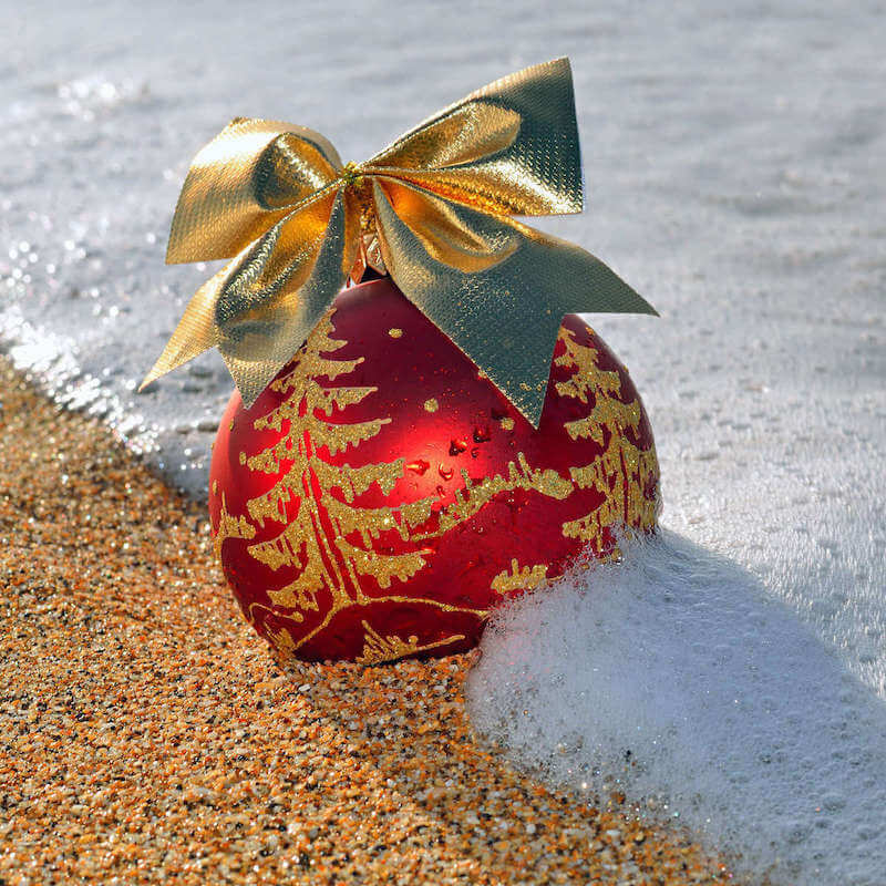 Find out all the best Hawaiian Christmas traditions by top Hawaii blog Hawaii Travel with Kids. Image of a Christmas ornament on the beach in Hawaii.