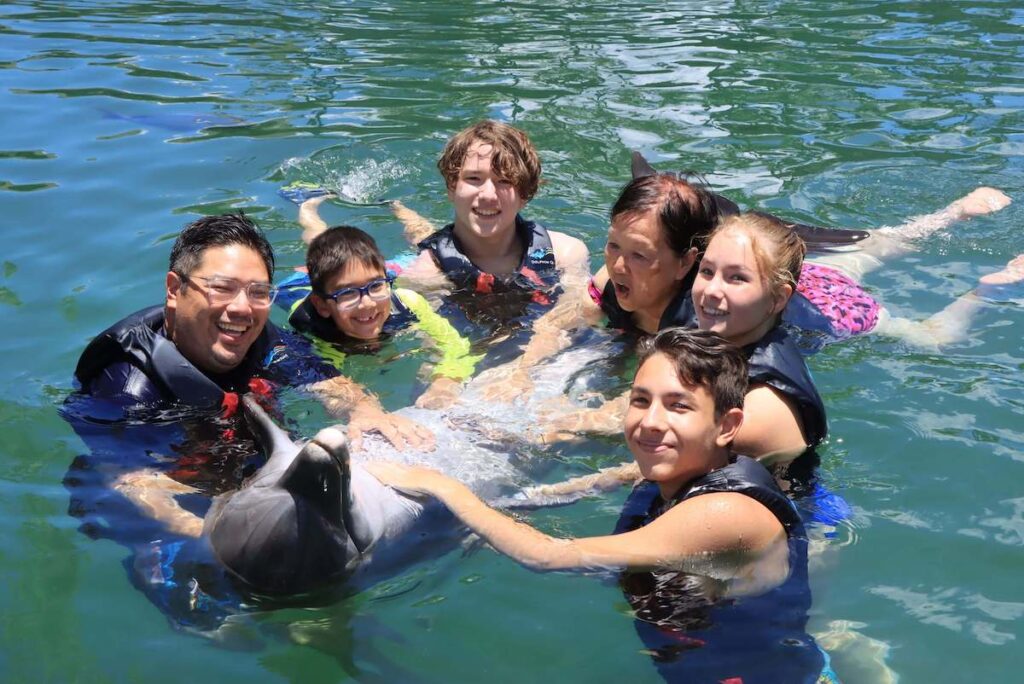 Want to swim with dolphins on Oahy? Read this Oahu Dolphin Quest review by top Hawaii blog Hawaii Travel with Kids. Image of a group of people with a dolphin