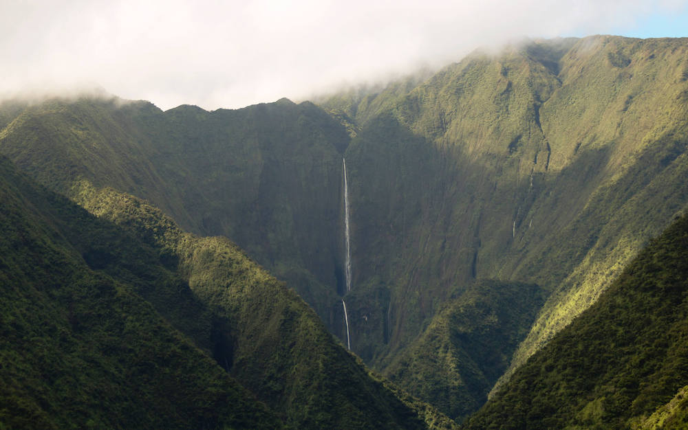 The tallest waterfall on Maui is Honokohau Falls. Image of a tall Maui waterfall surrounded by green mountains.