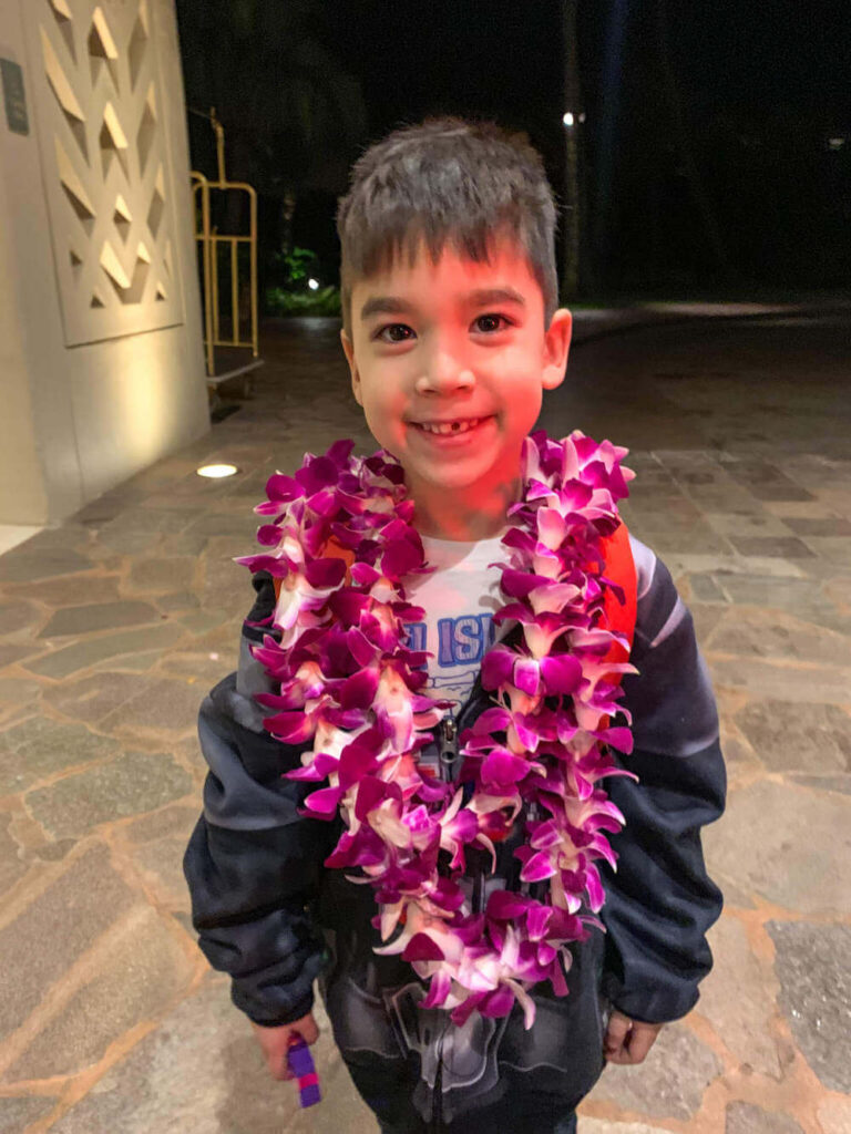 Read the full Grand Hyatt Kauai review by top Hawaii blog Hawaii Travel with Kids. Image of a boy wearing 2 purple leis.