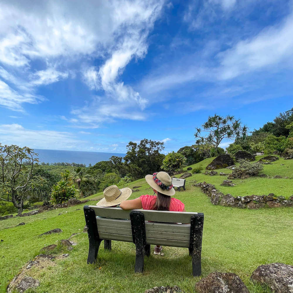 Should you explore the Limahuli Garden in Hanalei Kauai? Read this review by top Hawaii blog Hawaii Travel with Kids. Image of a boy and grandma sitting on a bench overlooking the ocean.