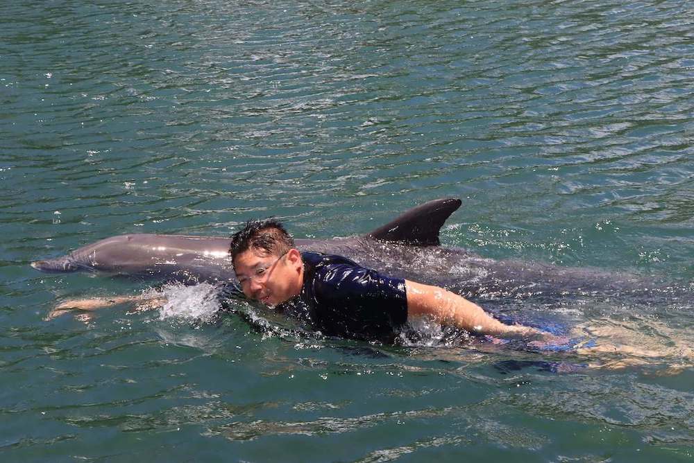 Image of a man wearing glasses swimming with a dolphin.