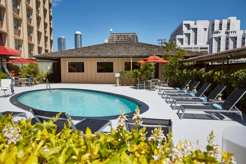 One of the cheapest places to stay in Waikiki is the Pagoda Hotel. Image of a small circular pool with some black lounge chairs.