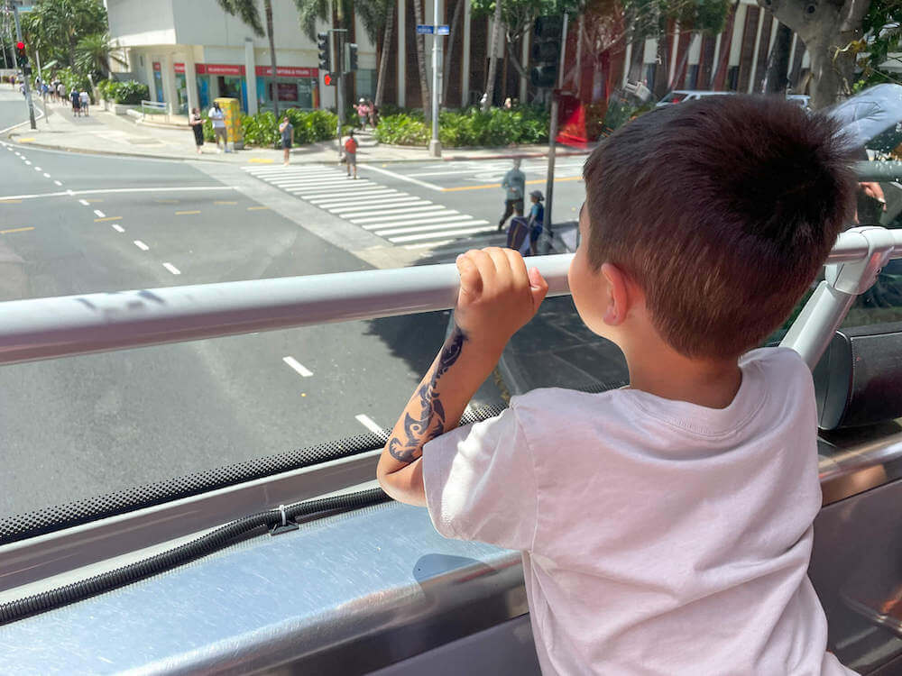 Find out whether the Waikiki Trolley is worth it for families. Image of a boy sitting on the front row of the upper deck of the Waikiki Trolley Pink Line.