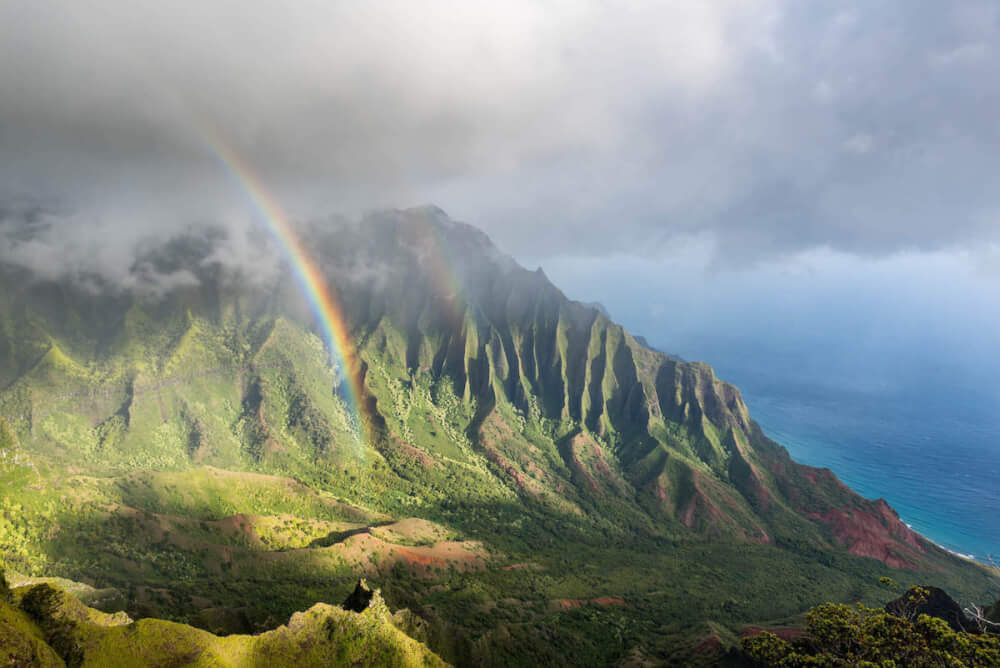 Find out the best things to do on Kauai when it rains by top Hawaii blog Hawaii Travel with Kids. Image of a rainbown over the Kalalau Valley on Kauai.