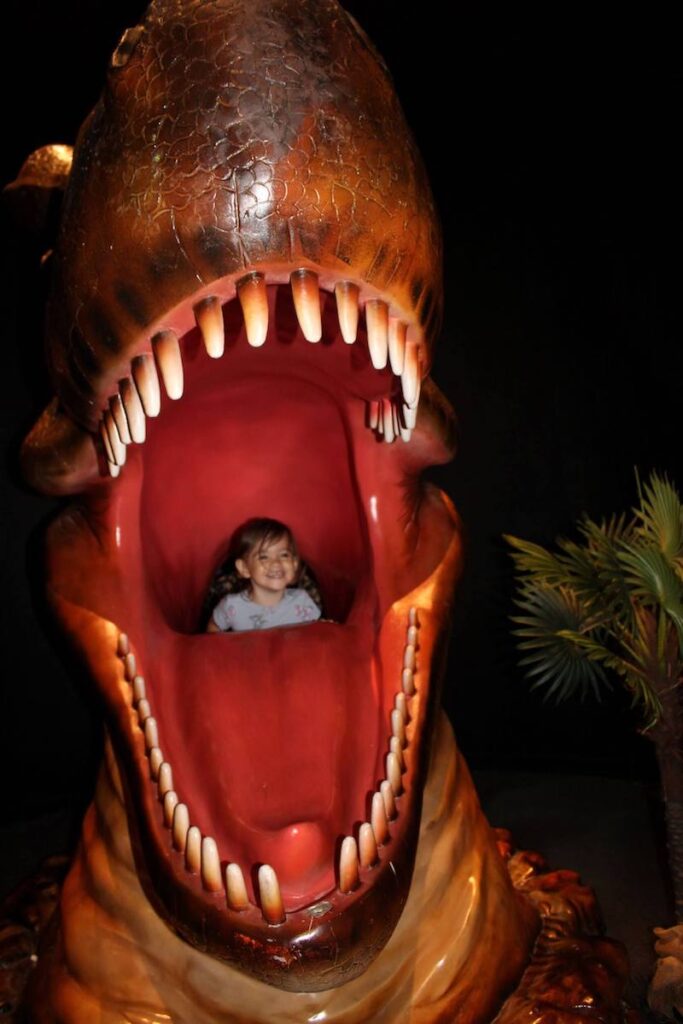 Image of a girl smiling inside a dinosaur's mouth at a Bishop Museum exhibit in Hawaii.