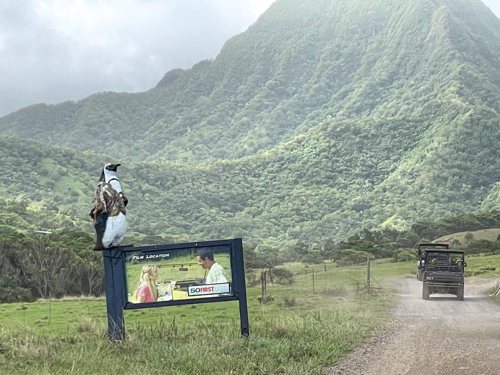 Image of a 50 First Dates sign at Kualoa Ranch with ATVs driving on a dirt road.