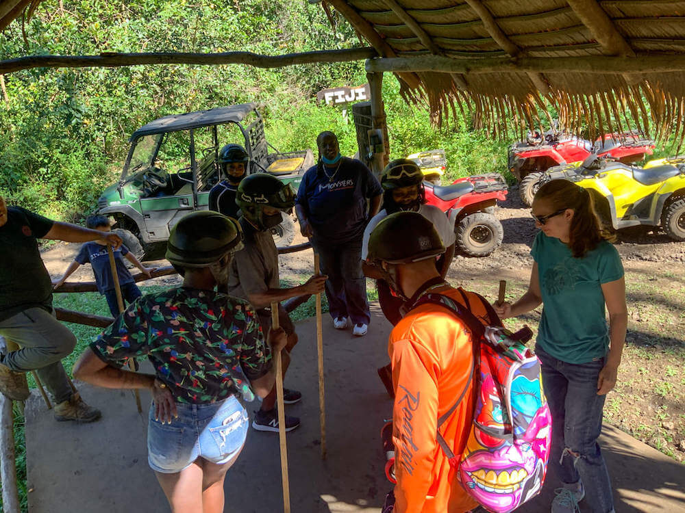 Image of a group of adults holding sticks inside a thatched building.