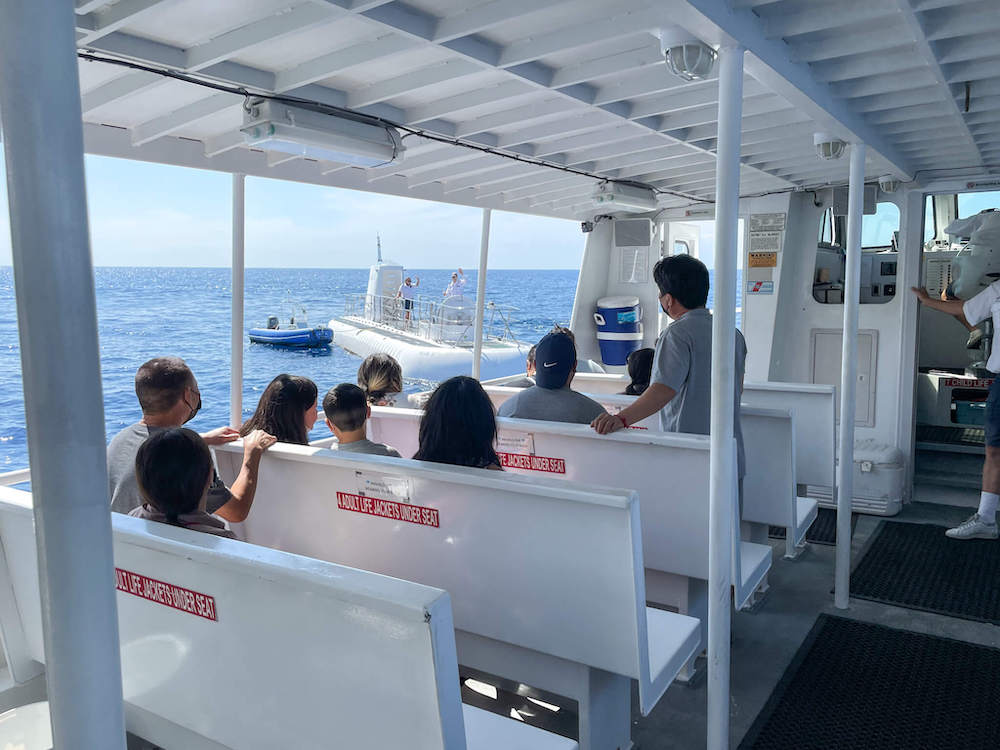 Image of the inside of a white boat with bench seating with a submarine in the background.