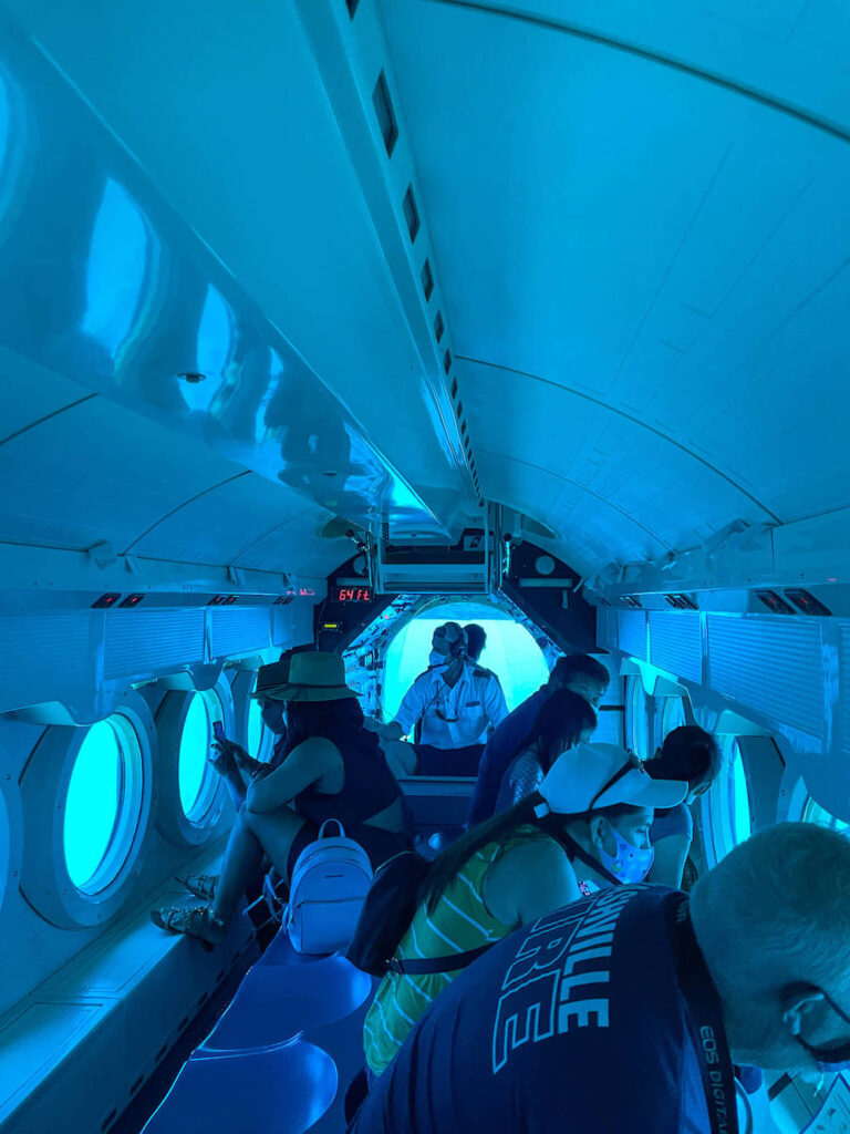 Image of the inside of a submarine with tourists looking out windows.