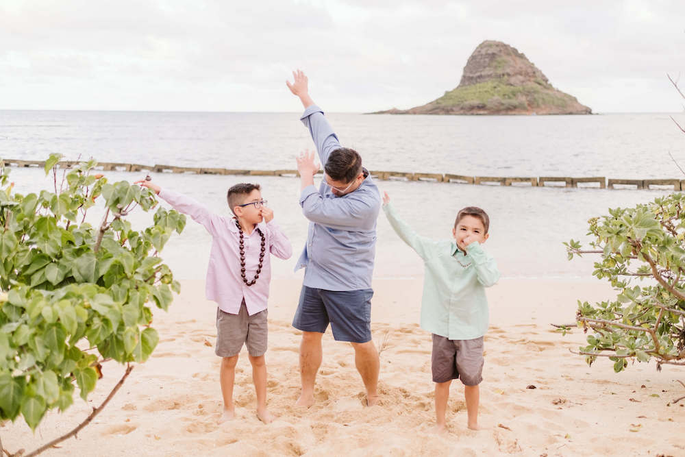 Image of a man and two boys dabbing on the beach in Hawaii.