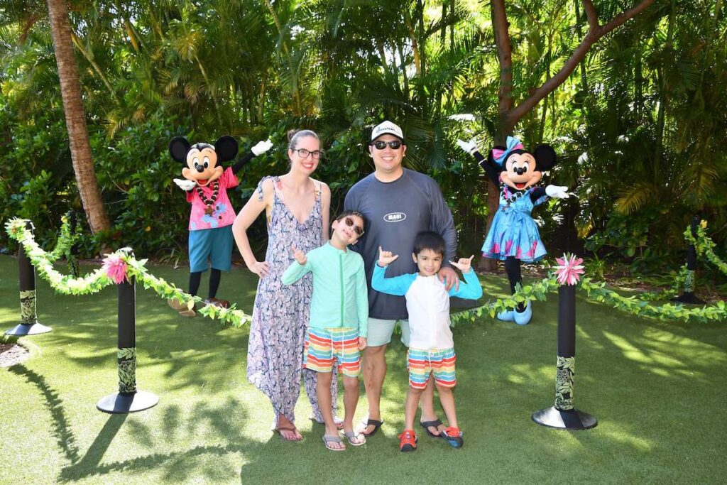 Find out how to meet characters at Disney Aulani Resort in Hawaii recommended by top Hawaii blog Hawaii Travel with Kids. Image of a family posing for a photo wiht Mickey and Minnie Mouse.