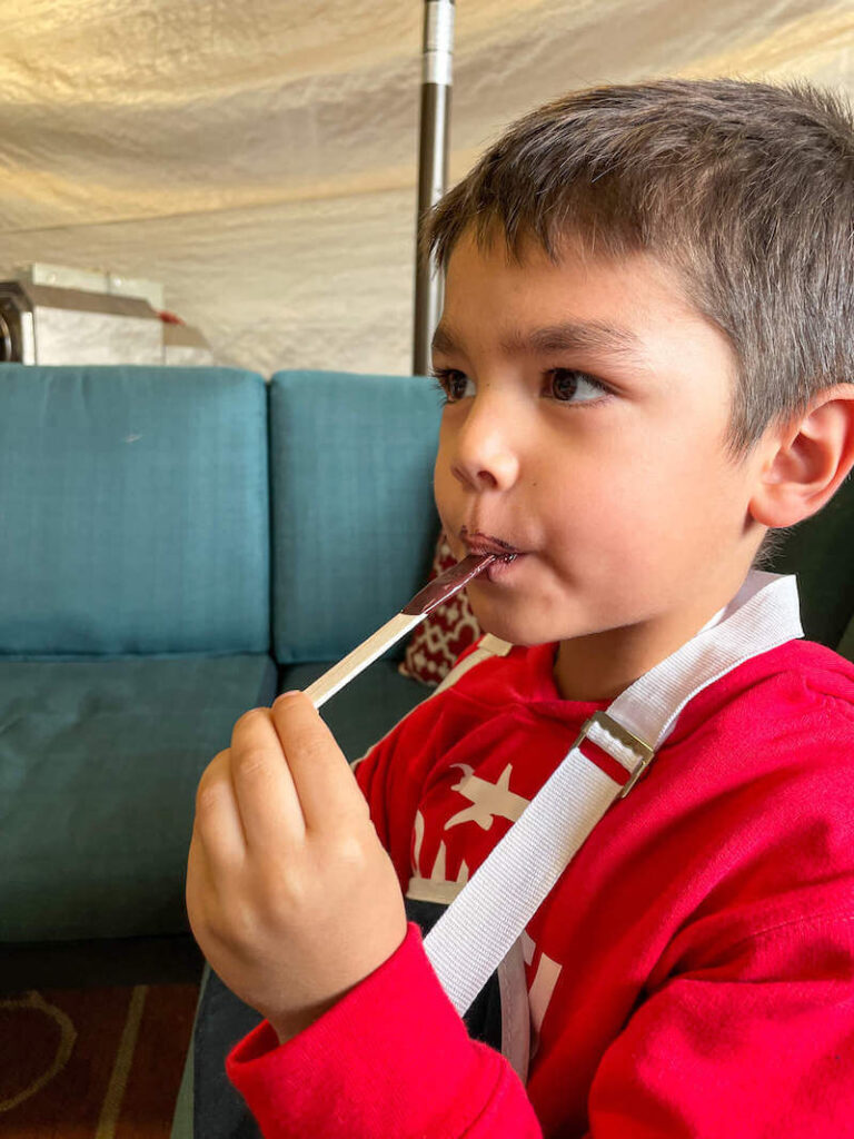 Image of a boy eating melted chocolate off a popsicle stick.