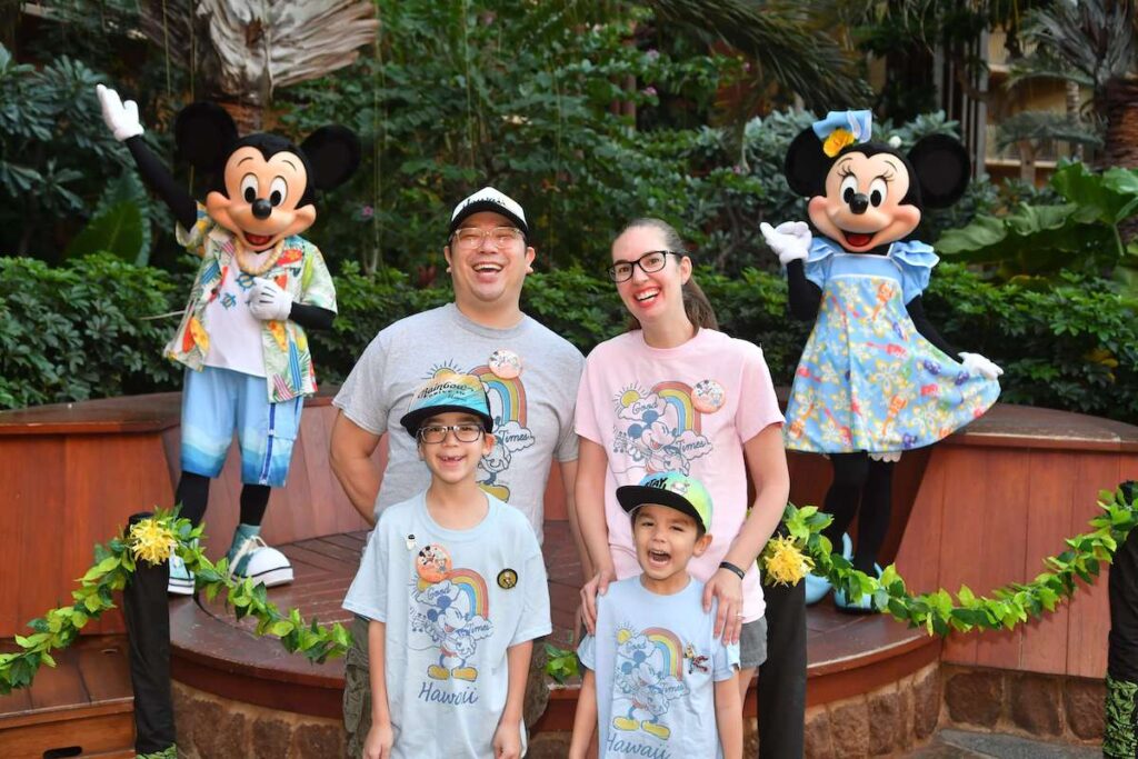 Image of a family laughing while wearing matching Aulani shirts with Mickey and Minnie in the background.