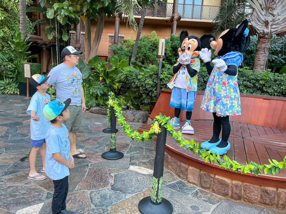 Image of Mickey and Minnie Mouse standing on stage laughing while talking to a man and two boys at Disney's Aulani Resort in Hawaii.