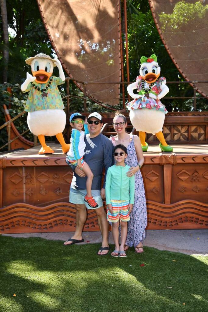 Image of a family posing with Daisy and Donald Duck dressed in Hawaiian clothing.