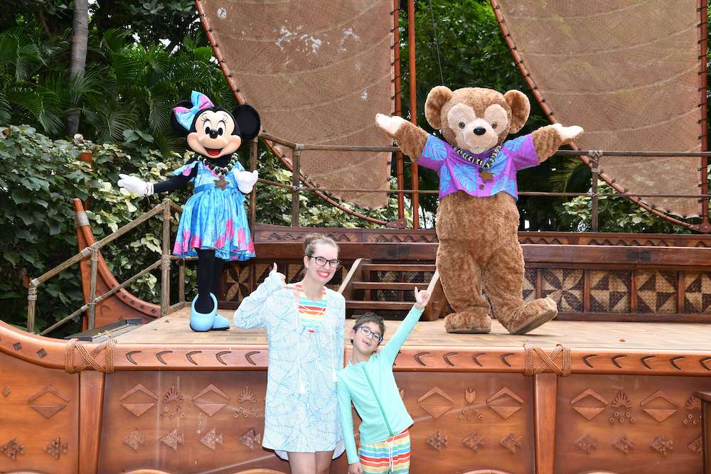 Image of a mom and boy posing with Minnie Mouse and Duffy, a brown teddy bear wearing a purple Aloha shirt.