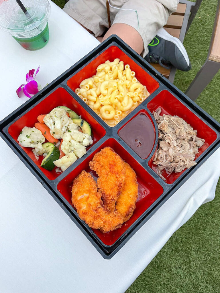 Image of a bento box with kalua pork, chicken nuggets, BBQ sauce, steamed veggies, and macaroni.