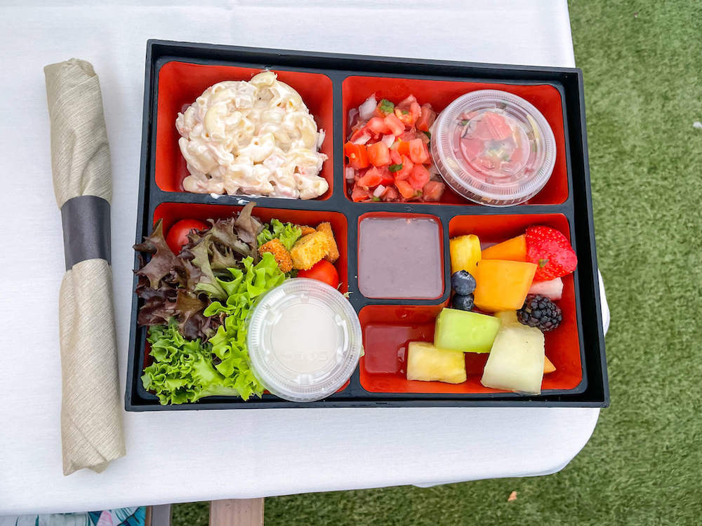 Image of a bento box with macaroni salad, poke, lomi lomi salmon, green salad, poi, and fresh fruit.