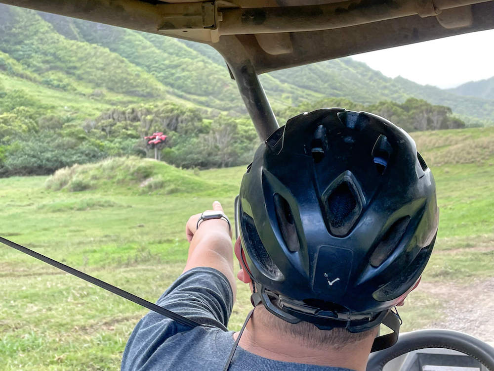 Image of a man wearing a helmet driving a UTV and pointing at two red ATVs at Kualoa Ranch in Hawaii.
