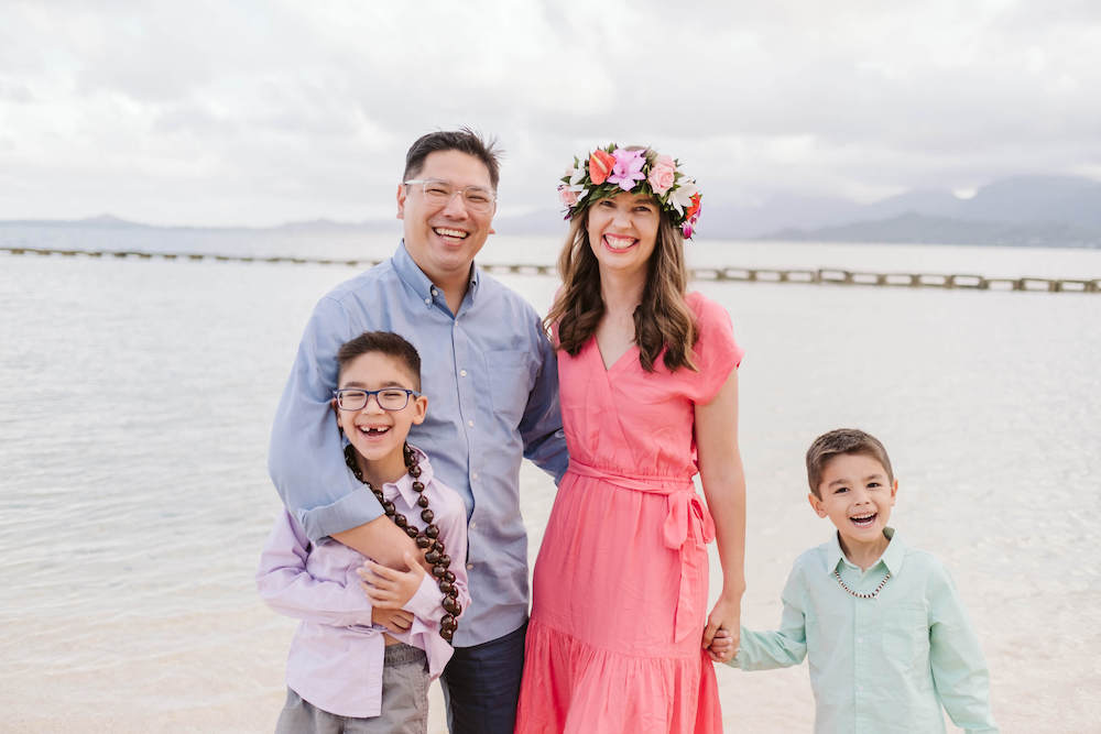 Image of a family dressed in rainbow colors posing for a photo in front of the ocean at Kualoa Beach on Oahu.