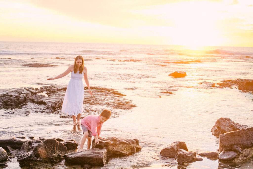 Old Kona Airport beach is one of the best places to see the sunset in Kona Hawaii. Image of a mom and son walking through a tidepool during sunset in Hawaii.