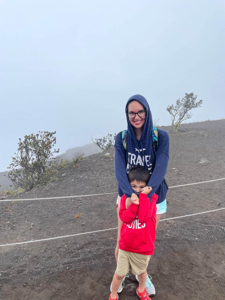 Image of a mom and boy standing at a scenic lookout at Hawaii Volcanoes National Park with fog in the background so you can't see the scenery.