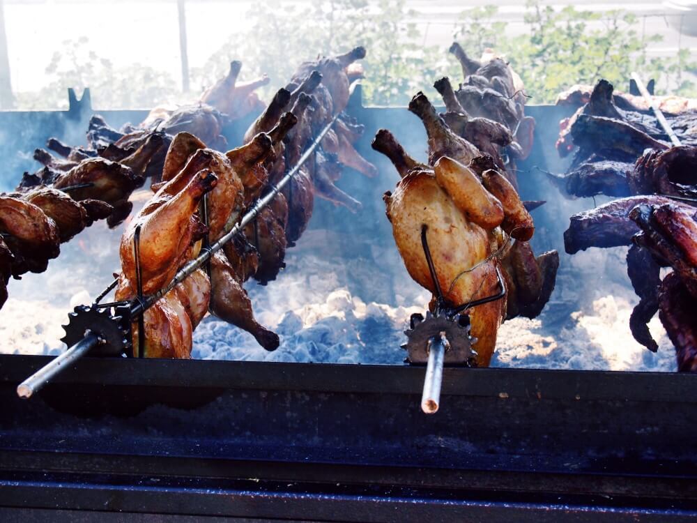 Image of a bunch of whole chickens on spits over hot coals.