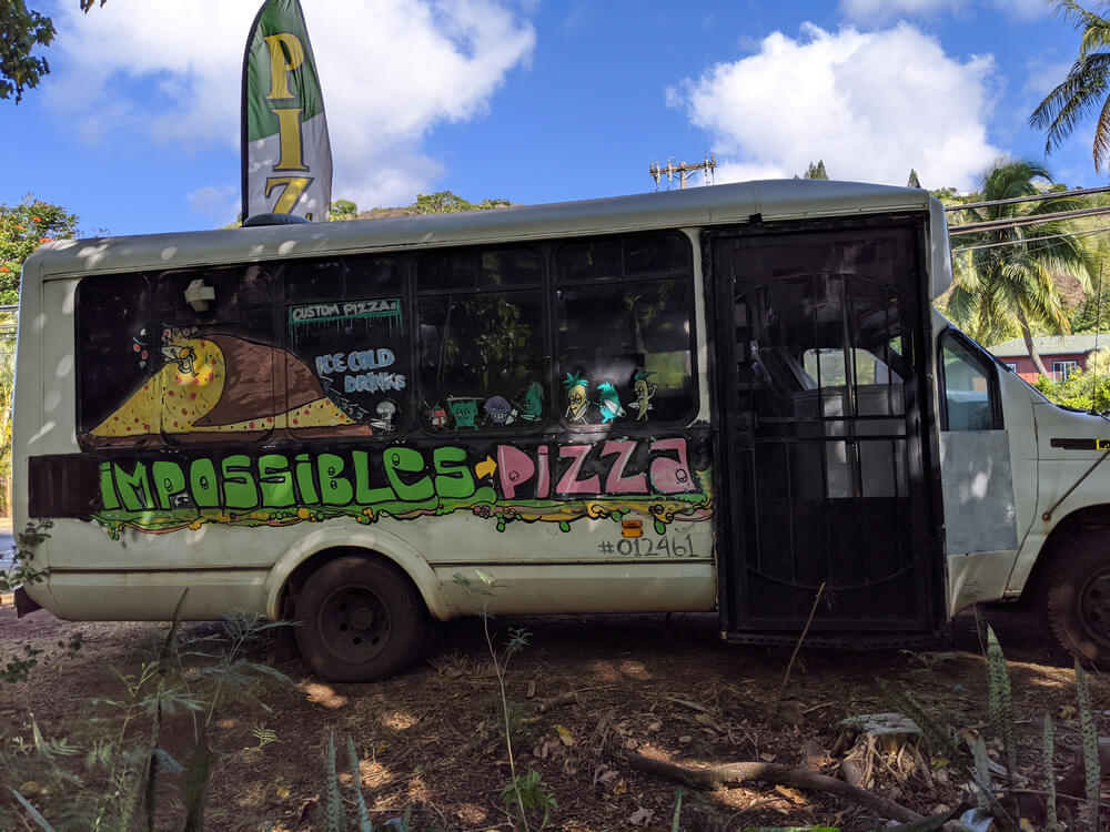 Image of a run down tour bus with the name Impossibles Pizza painted on the side.