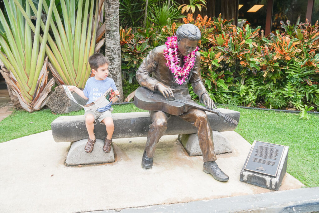 Image of a boy sitting next to a statue of a man playing the steel guitar.
