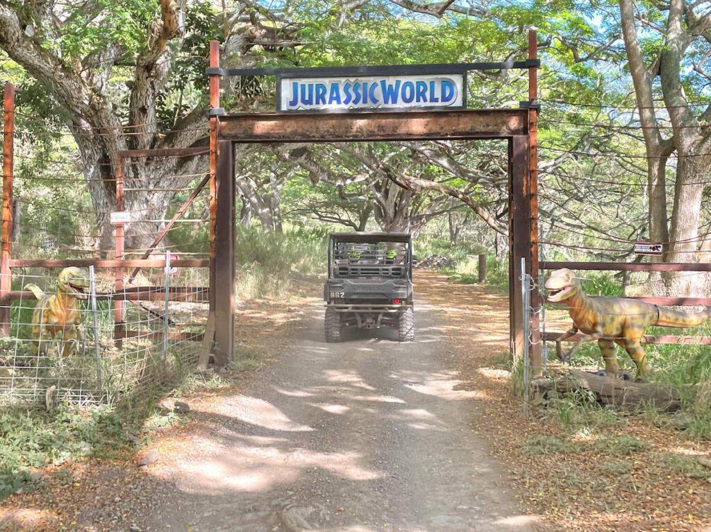 Image of a UTV driving into Jurassic World movie site with fake dinosaurs surrounding it.