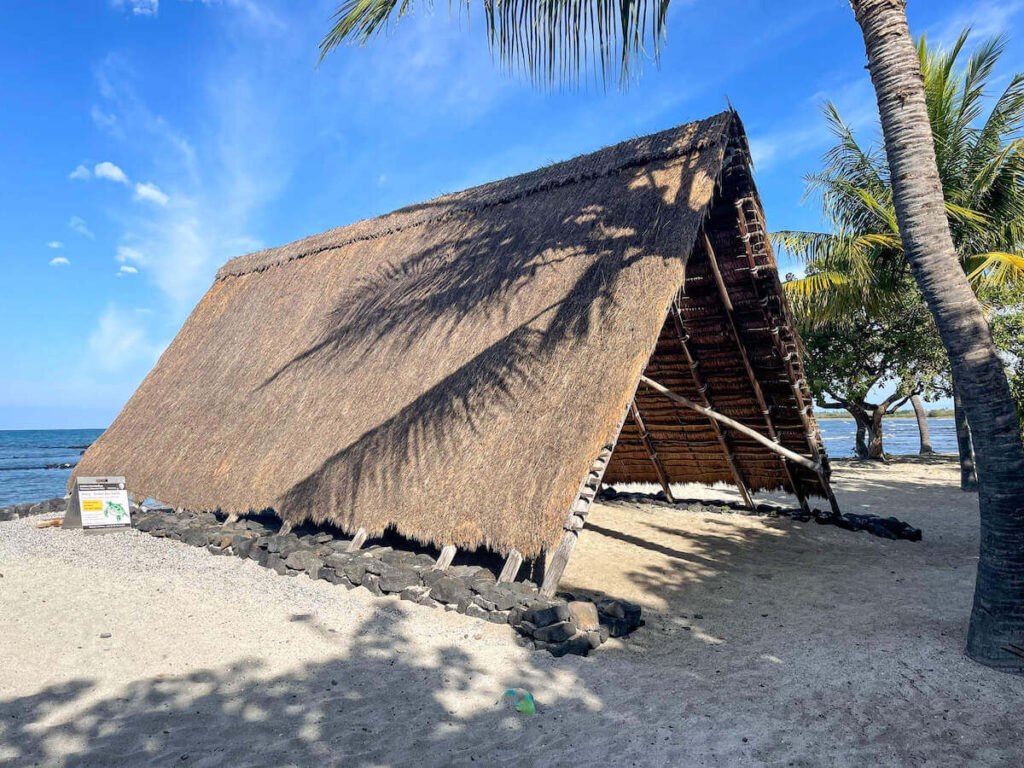Find out whether or not to explore Kaloko-Honokohau National historical park by top Hawaii blog Hawaii Travel with Kids. Image of a large Hawaiian hut on the beach by the ocean in Kona, Hawaii.