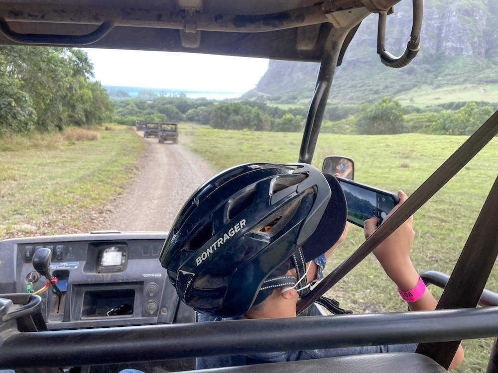 Image of a boy sitting in a UTV wearing a helmet taking photos with a cell phone at Kualoa Ranch in Hawaii.