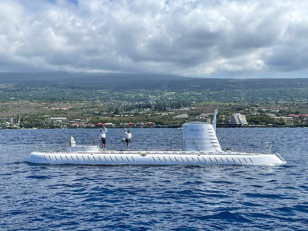 Image of crew members waving on top of a white submarine in Kona Hawaii.