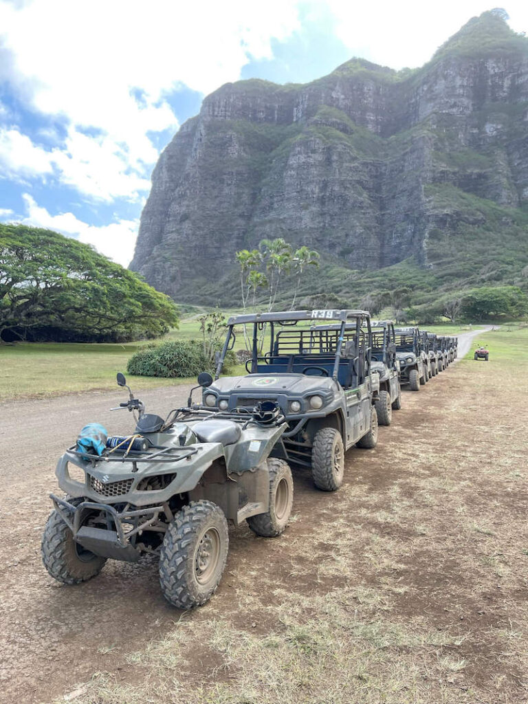 One of the best things to do on Oahu with kids is this Jurassic Valley ATV tour on Oahu. Image of a line of ATVs and UTVs at Kualoa Ranch in Hawaii.