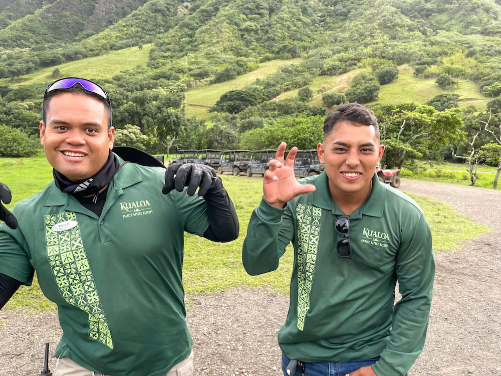 Image of two young men wearing green Kualoa shirts pretending to be dinosaurs in Hawaii.