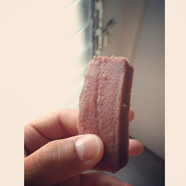 Image of someone holding up a rectangular piece of kulolo, a Hawaiian dessert.