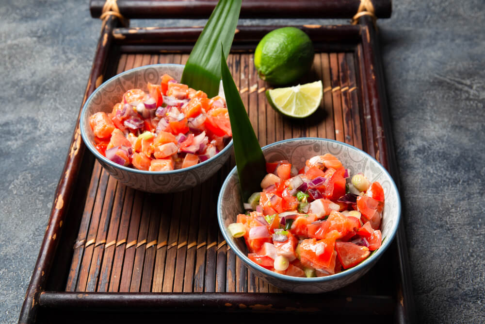 Image of chopped up raw salmon with tomatoes and onions in two bowls.