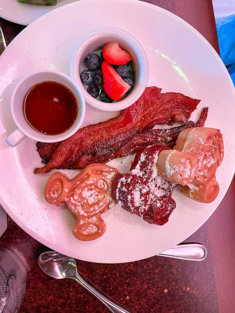 Image of a plate of Mickey waffles, bacon, fruit, and syrup at the Aulani character breakfast.