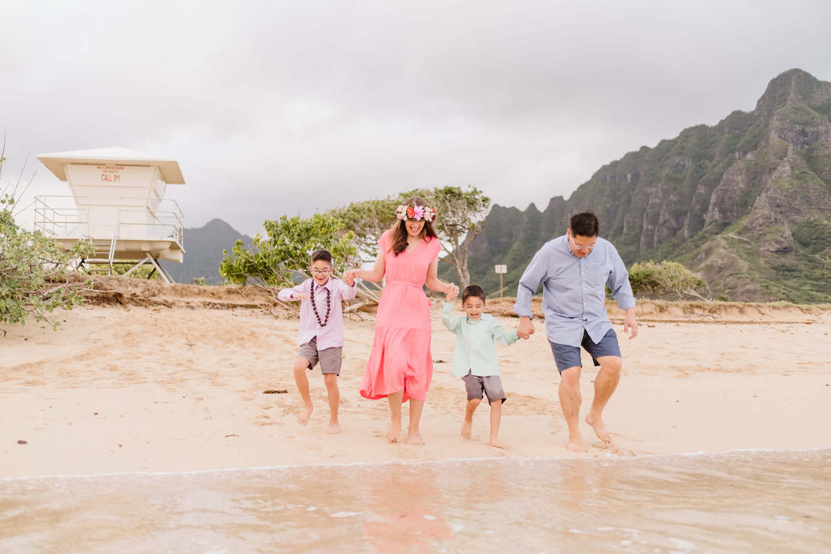 Find out how to book Oahu family photography sessions by top Hawaii blog Hawaii Travel with Kids. Image of a family standing near the water at Kualoa Beach Park on Oahu
