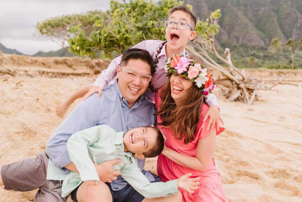 Image of a family dressed up and tickling each other while on a beach in Oahu Hawaii